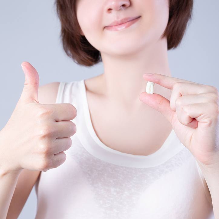 Nose-to-chest view of woman holding extracted tooth and giving thumbs up